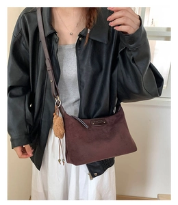 Detail of dark brown suede crossbody bag featuring a metal logo plate and plush bear charm