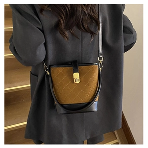 Detail of suede bucket bag with quilted patterns and gold twist-lock closure worn by model