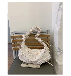 Détail du sac à fleurs avec des nœuds latéraux et une poignée au design froncé