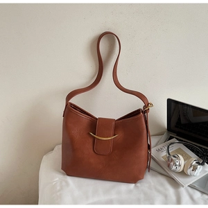 Close-up of brown tote bag with gold curved metal buckle and smooth leather texture
