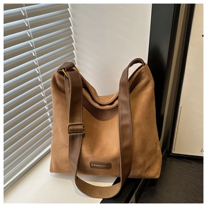 Detail of brown faux suede tote bag featuring a leather brand tag and gold metal buckle