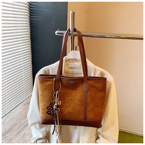 Detail of caramel suede tote bag with brown leather trim and bear pendant decoration