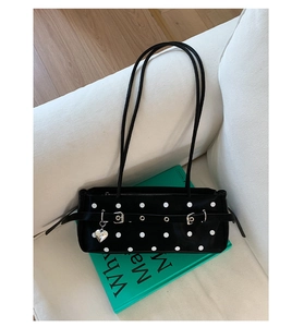 Detail of a black polka dot underarm bag with silver heart charm on green books