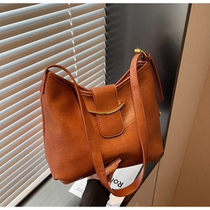 Detail of a brown leather shoulder bag featuring a gold crescent moon metal buckle