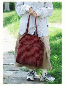 Detail of red and black houndstooth knit tote bag held by a model in outdoor setting
