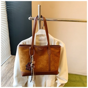Close-up of vintage brown suede tote bag with scarf and bear charm on a white blazer
