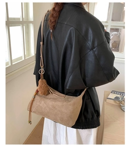 Close-up of camel suede crossbody bag featuring brown plush ball and colorful bead charms