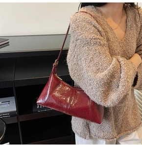 Detail of burgundy patent leather baguette bag with triangular texture and gold hardware