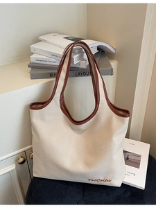 Minimalist oatmeal canvas tote bag with brown leather trim on a textured black velvet chair