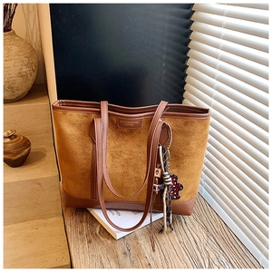 Close-up of a brown suede tote bag featuring a teddy bear charm and logo detail