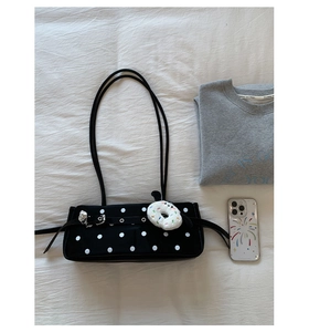 Close-up of black polka dot underarm bag with decorative metal eyelet strap and plush charm