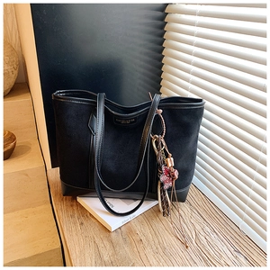 Detail of black suede tote bag with leather trim, fashion text and bear charm accessory