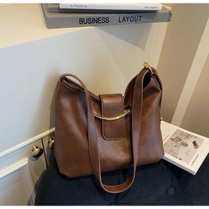 Detail of a dark brown matte leather tote bag with gold curved metal accent and magnetic flap
