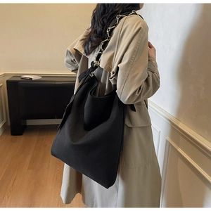 Détail d'un grand sac hobo noir en daim avec une bandoulière en chaîne dorée chic
