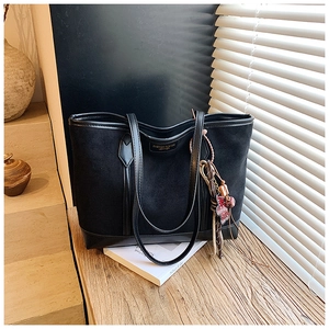 Detail of black matte tote bag with polished handles and vintage flower bag charm
