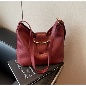Close-up of burgundy leather tote with a gold half-moon buckle on black art books