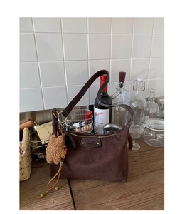 Détail du sac bandoulière en daim marron foncé avec plaque logo et breloque en ours