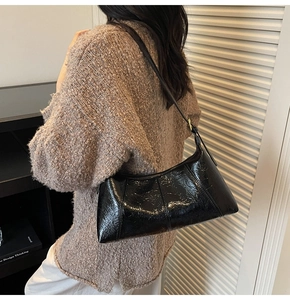 Detail of black glossy crinkled leather handbag with adjustable golden buckle strap