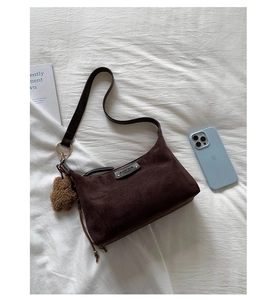 Détail du sac en daim marron foncé avec breloque ours en peluche et logo en cuir