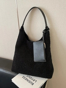 Large black plush faux fur tote bag with matching leather pouch on a textured wall