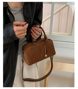Close-up of suede Boston bag with silver heart pendant and knotted handle detail