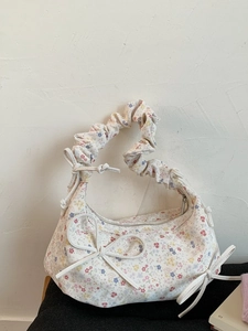Sac à main floral avec poignée froncée et nœuds décoratifs sur un coussin noir