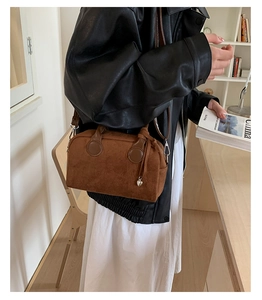 Close-up of brown suede pillow bag with silver heart charm on model in leather jacket