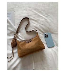 Gros plan du sac bandoulière vintage en daim marron avec pendentif ours sur tissu blanc