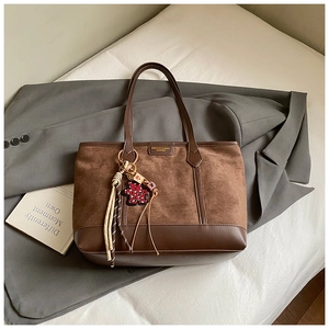 Detail of brown patchwork tote bag with cute bear charm and tassel on grey blazer