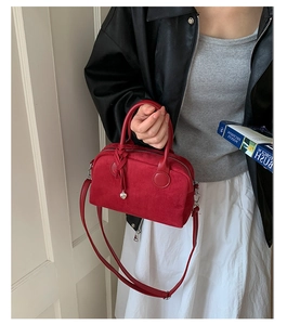 Detail of red suede Boston bag held by model featuring heart pendant and leather strap