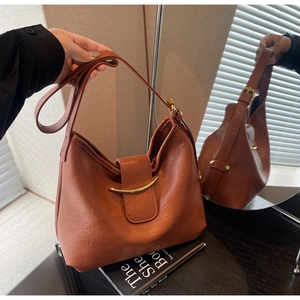 Detail of brown leather tote bag featuring a decorative gold curved metal accent bar