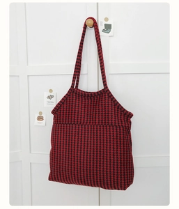 Detailed close-up of a red and black houndstooth tote bag on a wooden wall hook