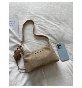 Détail du sac à bandoulière en daim avec logo en métal et breloque ours sur tissu blanc