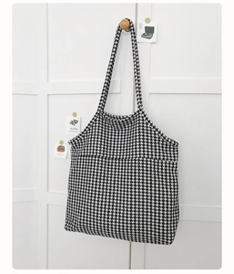 Detail of black and white houndstooth knit tote bag hanging on a minimalist wall hook