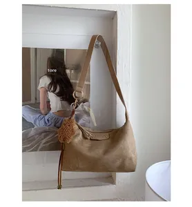 Détail du sac en daim camel avec étiquette logo, pendentif ours et décoration pompon