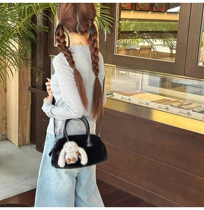 Detail of a fluffy black crossbody bag with a cute white bunny charm and leather handles