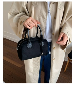 Detail of black plush bowling bag with round handles shown in a lifestyle street setting