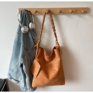 Sac hobo en daim caramel avec bandoulière tressée et petite pochette sur un cintre en bois