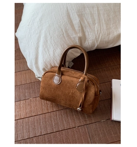 Detailed view of brown suede pillow handbag with soft leather handles and heart tassel charm