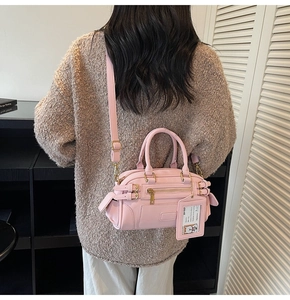 Detail of pink faux leather boston bag featuring cylindrical handles and adjustable strap