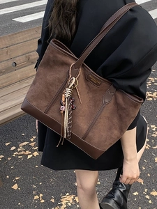 Large dark brown suede tote bag with leather straps worn by a model in a street setting