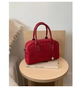 Detail of red suede Boston bag with leather handles and silver heart charm pendant