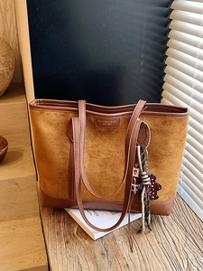 Retro brown large-capacity tote bag in matte leather shown on a wooden desk with a doll pendant