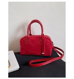 Close-up of red suede Boston bag with silver heart pendant on a velvet surface