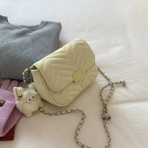 Detailansicht der beigen Stepptasche mit Metallkettenriemen und flauschigem Anhänger
