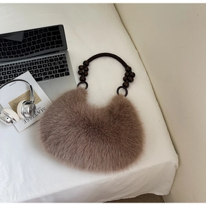 Detail of a brown fuzzy faux fur crescent bag with decorative beaded handle on a white desk