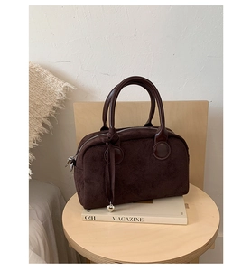 Detail of dark brown suede Boston bag with silver heart pendant on a wooden stool
