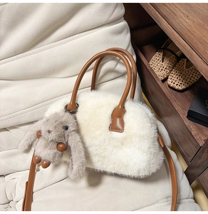 Detailed view of a white fuzzy faux fur handbag with brown leather straps and bunny charm