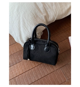 Detail of black suede hobo bag with leather handles and silver ball charm on wooden floor