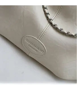 Détail du sac en cuir crème montrant la chaîne métallique et le logo de marque embossé